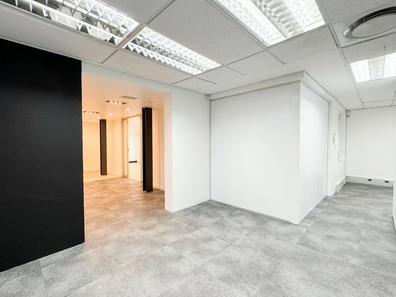 A modern, vacant office space featuring neutral tiled flooring, clean white partition walls, and a suspended ceiling with recessed lighting.
