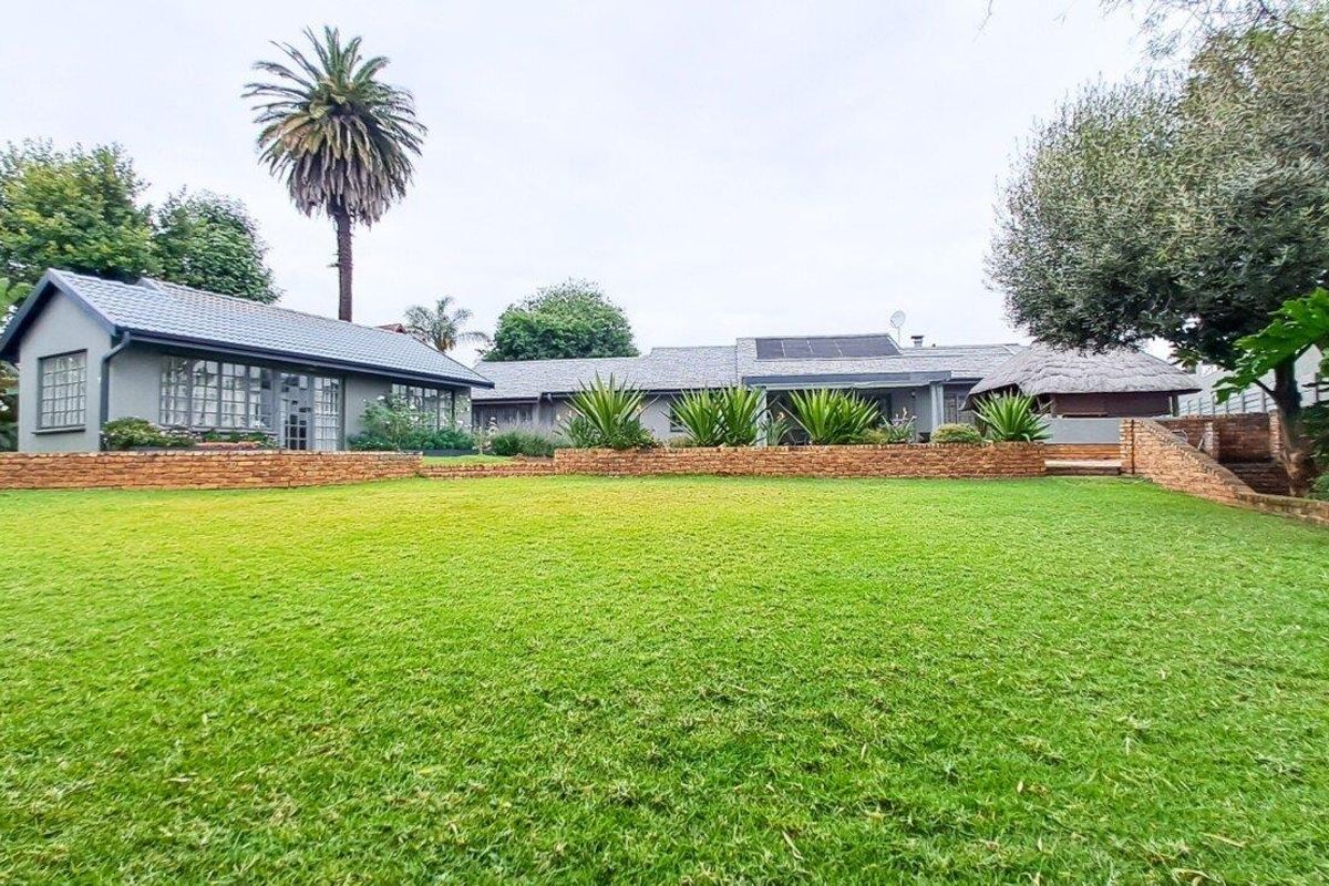 Spacious rear garden featuring a well-maintained lawn, brick retaining walls, and a view of the main residence with solar panels and a thatched roof area.