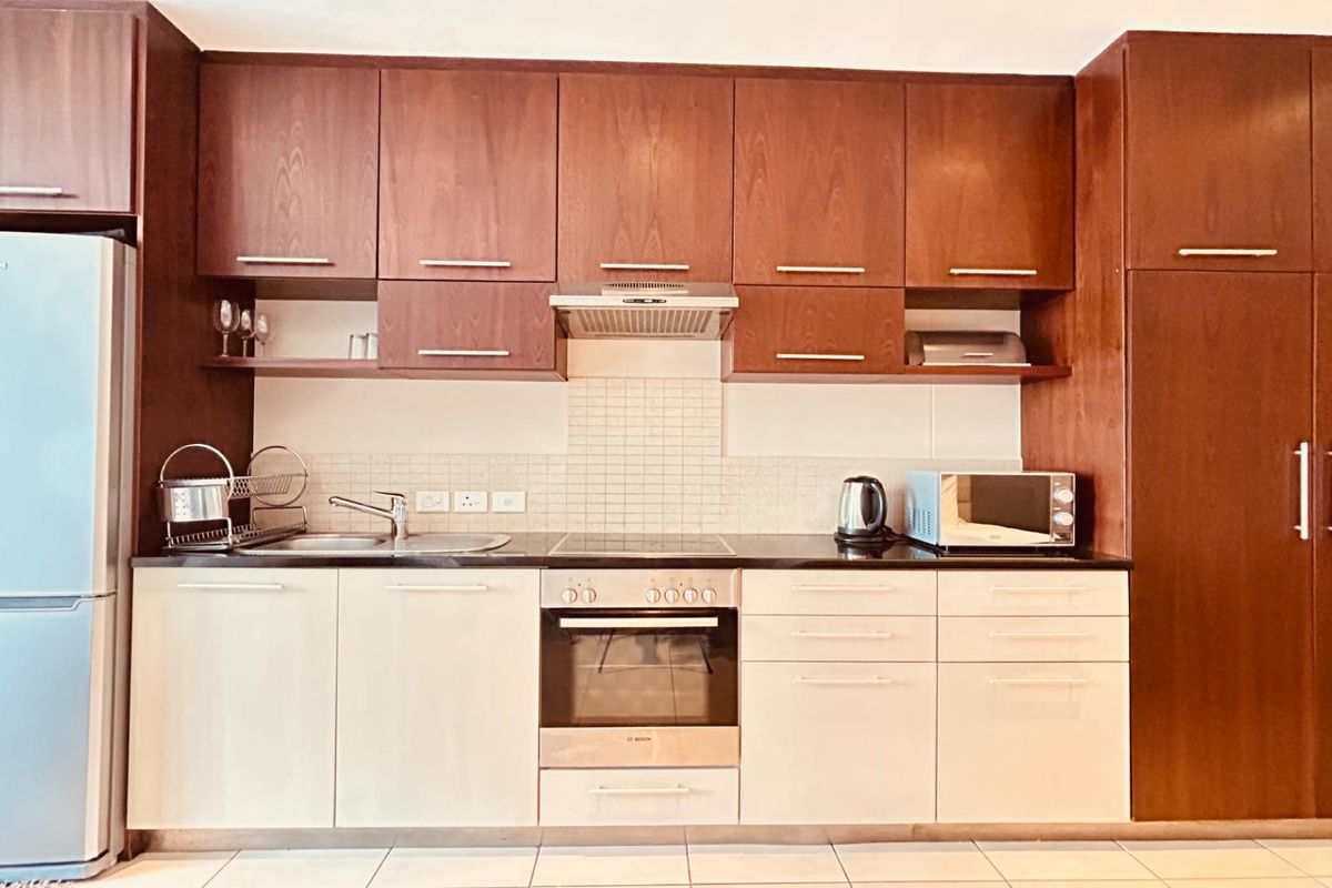 A functional kitchen featuring dark wood upper cabinetry, light lower cabinets, stone countertops, and integrated appliances including an oven and extractor fan.