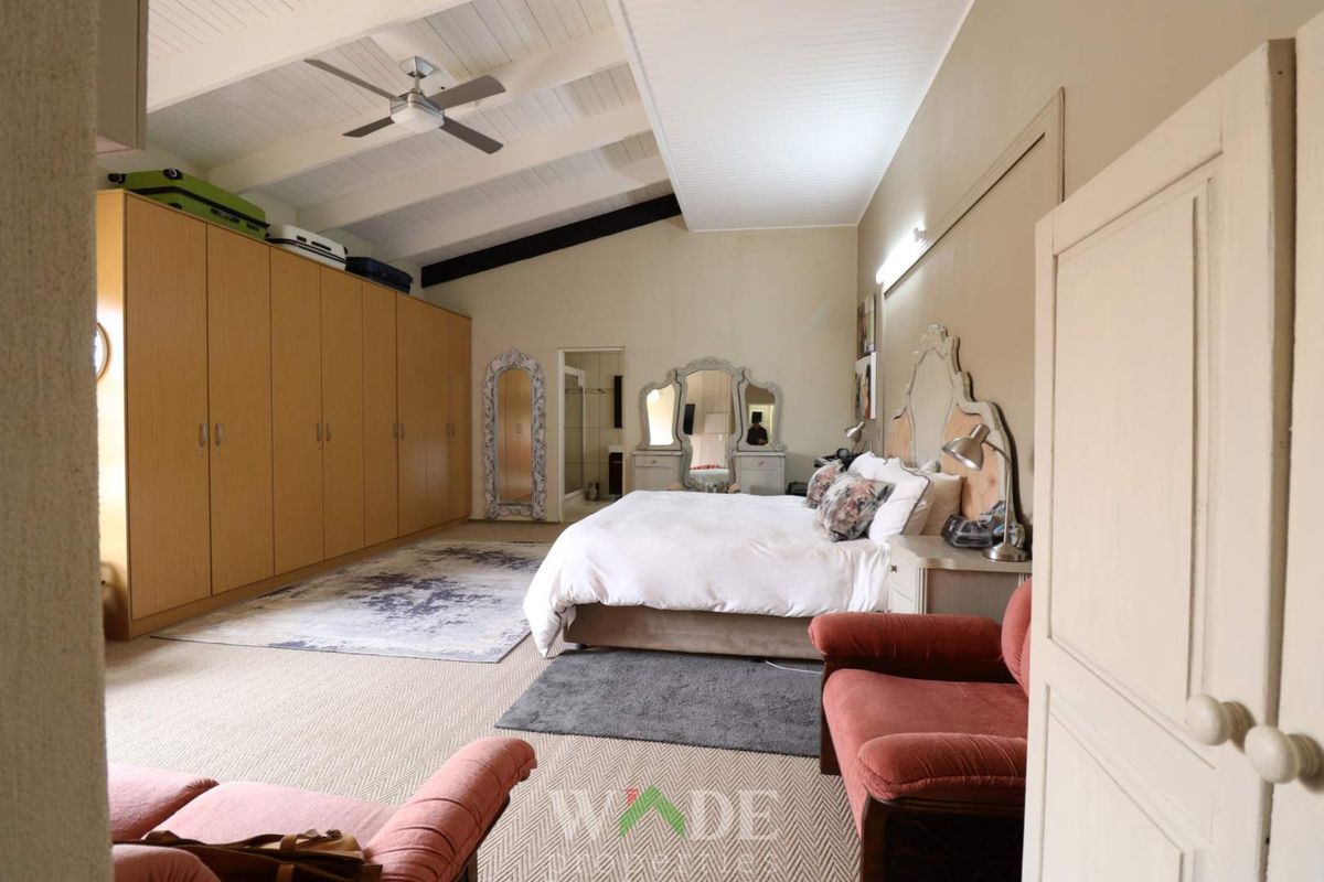 Spacious bedroom featuring high vaulted ceilings with exposed beams, a ceiling fan, and extensive built-in wardrobe cabinetry.