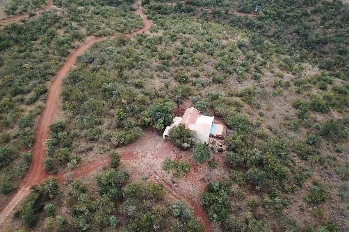 Aerial view of a secluded residential property nestled within a natural bushveld landscape, featuring a private swimming pool and surrounding dirt access tracks.