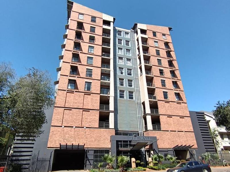Front elevation of The Wall apartment building, featuring a modern brick facade, integrated balconies, and secure ground-level parking access.
