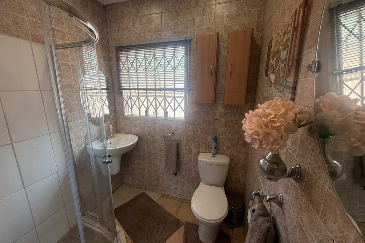 A functional bathroom featuring a shower enclosure, pedestal basin, toilet, and wall-mounted cabinetry with neutral tiled finishes throughout.