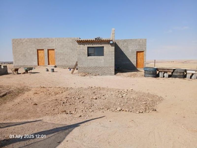 Rear view of a small holding property showing an unfinished concrete block structure with wooden doors and exposed exterior surfaces.
