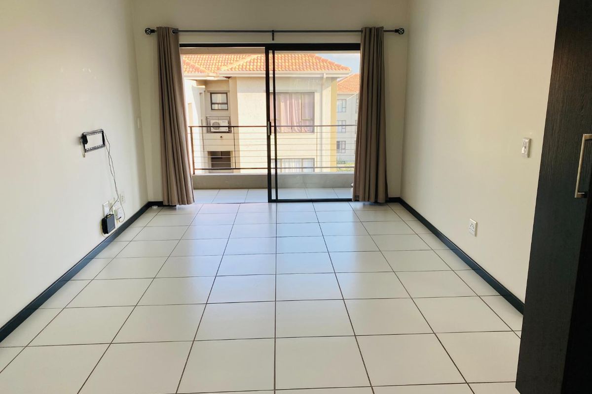 An empty, well-lit living area featuring neutral tiled flooring and a sliding glass door providing direct access to a private balcony.