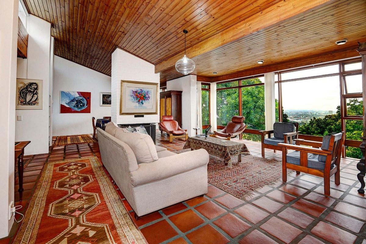 Spacious living area featuring a vaulted timber-clad ceiling, terracotta tiled flooring, a central white brick fireplace, and expansive floor-to-ceiling windows with scenic views.