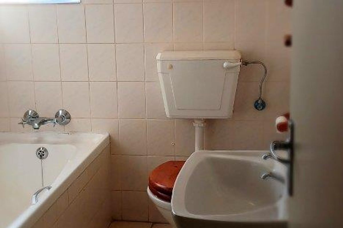A functional bathroom featuring a pedestal basin, a standard bathtub with shower mixer, and a wall-mounted toilet.