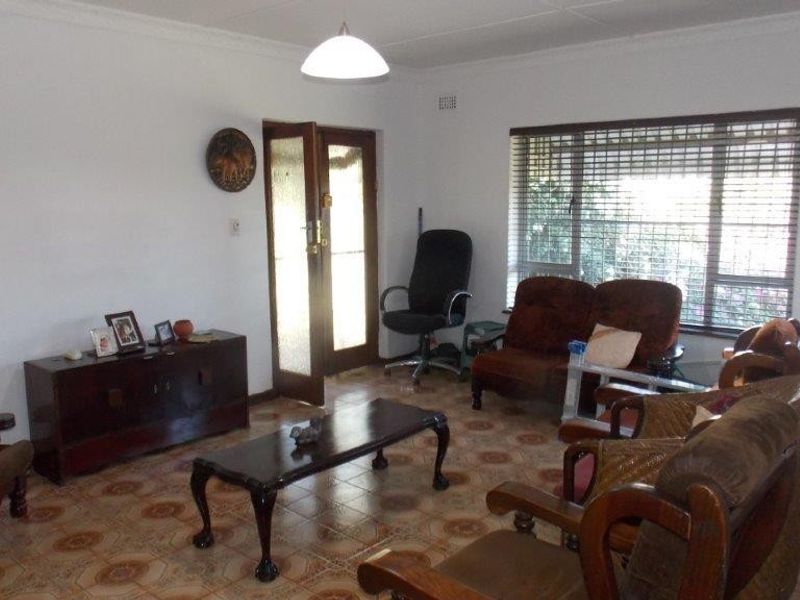 A living room featuring tiled flooring, large windows with blinds, and a timber-framed entrance door.