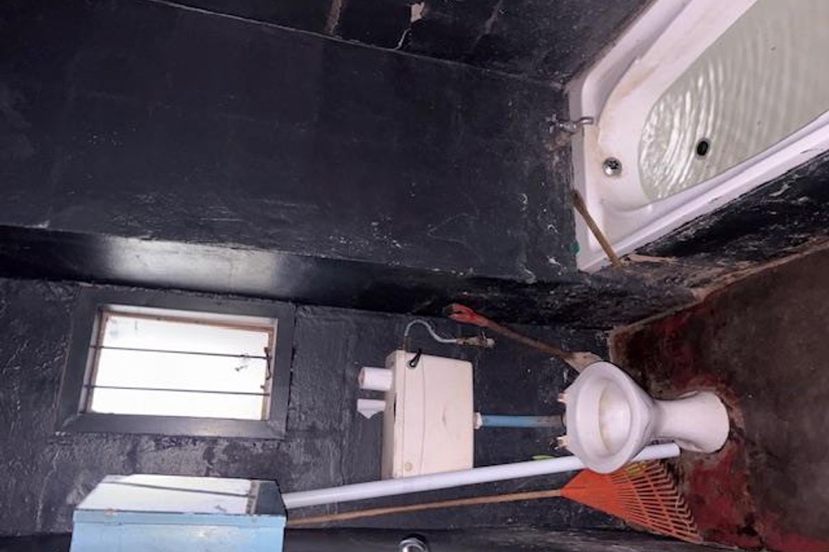 A bathroom space requiring significant renovation, featuring a bathtub, toilet, and basic window, currently in a state of severe deterioration.