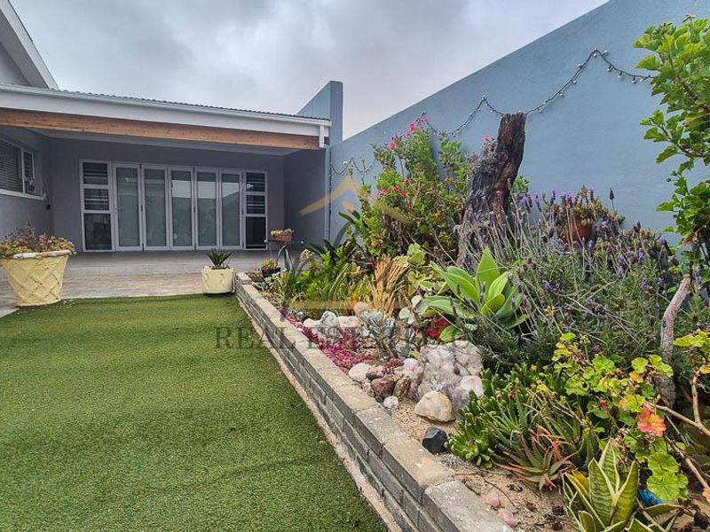 A well-maintained rear garden featuring an artificial lawn, a raised brick garden bed with established plants, and a covered patio area with sliding doors.