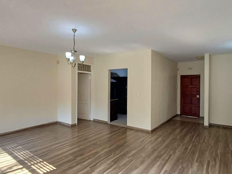 Spacious, empty living area featuring laminate flooring, neutral walls, and direct access to the front entrance and adjacent kitchen area.