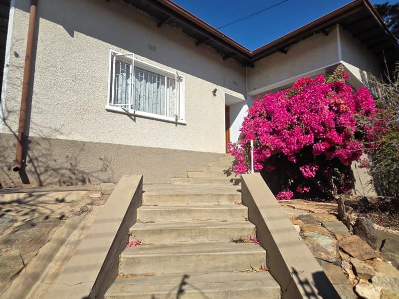 Front exterior view of the house featuring a concrete staircase leading to the entrance, complemented by a large flowering bougainvillea bush.