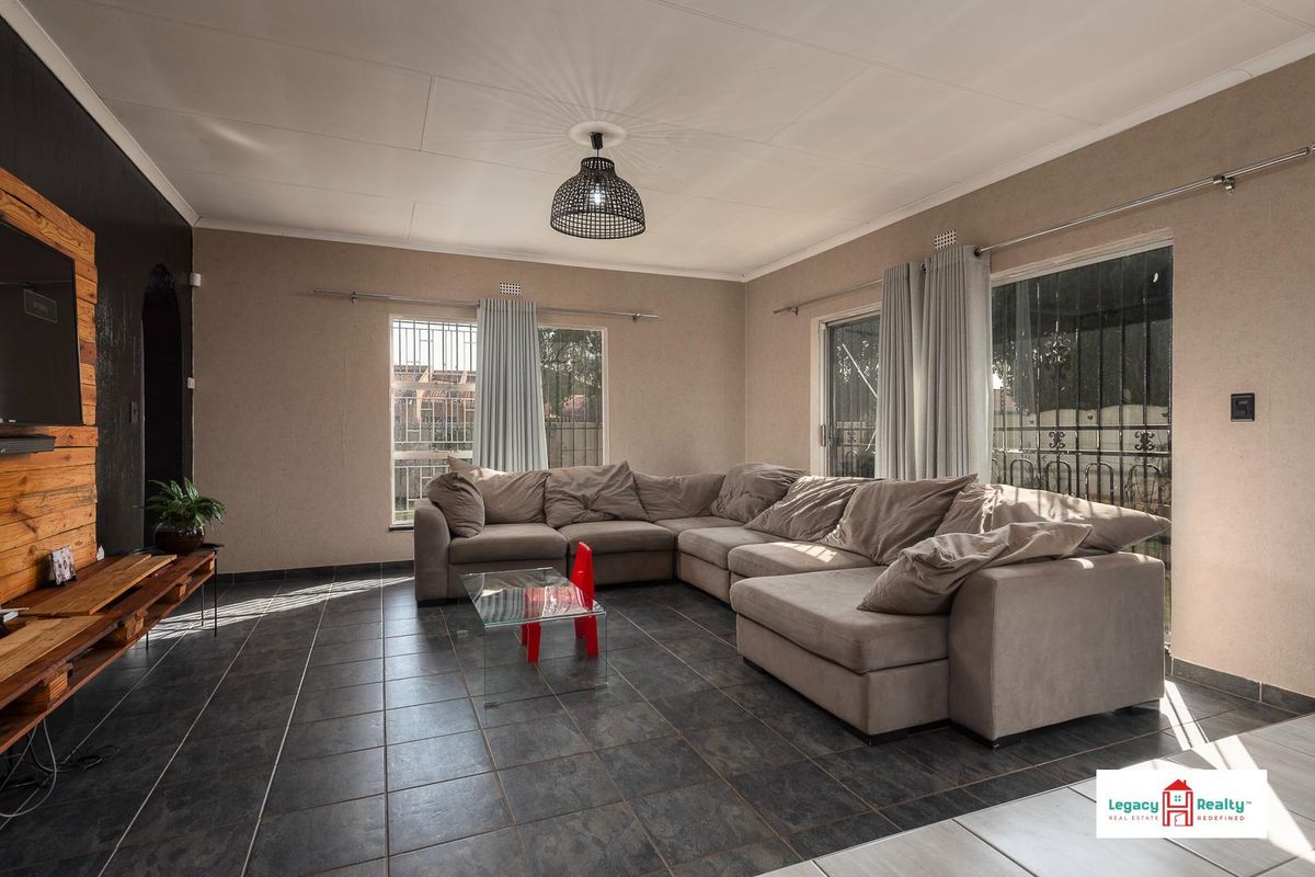 Spacious living room featuring dark tiled flooring, large windows with security bars, and a feature wall with wood paneling.