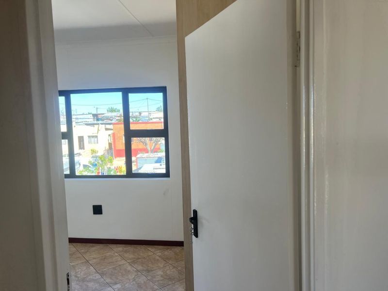 A bright, empty bedroom featuring tiled flooring and a large aluminium-framed window, offering a clear view of the surrounding neighbourhood.