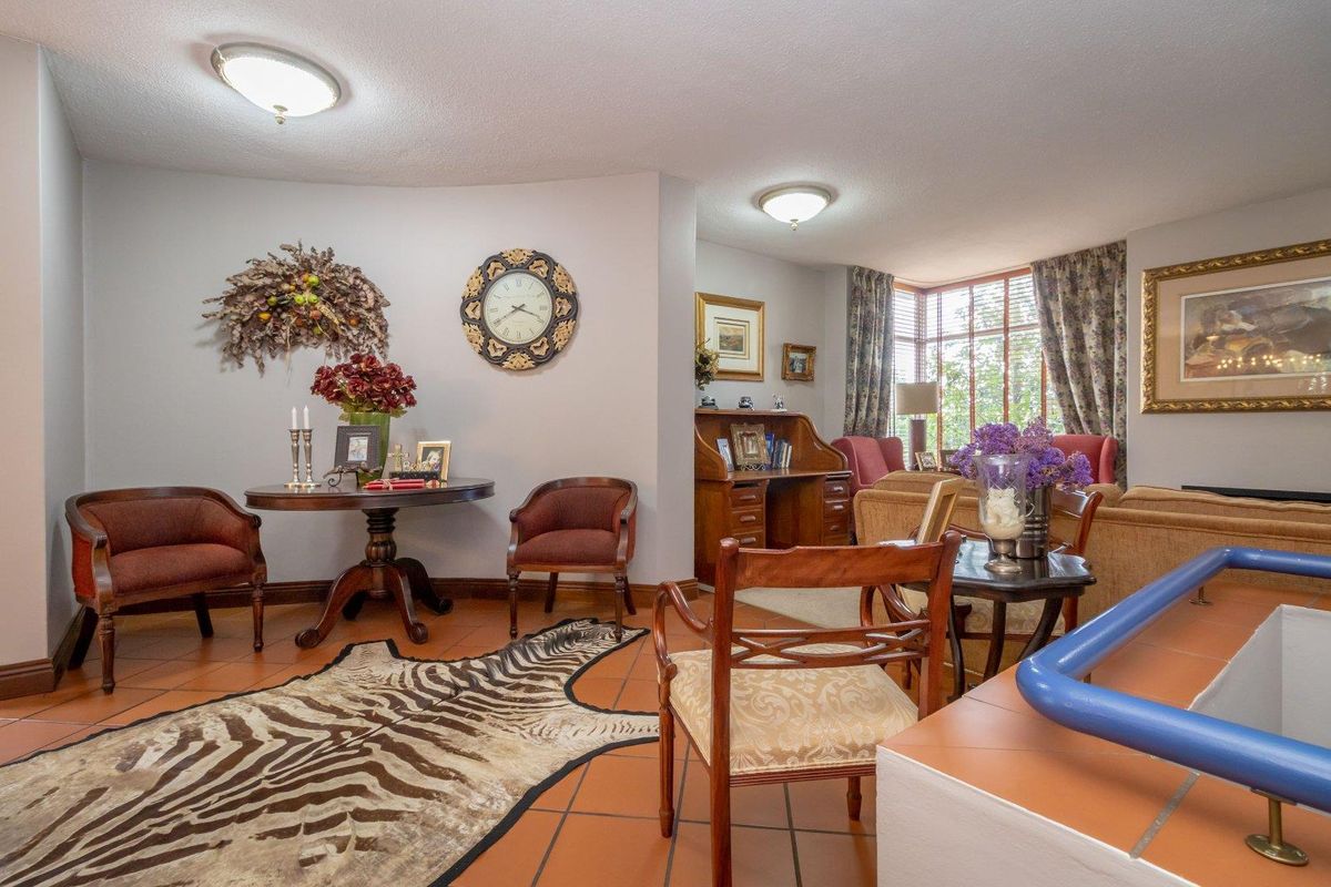 A spacious living area featuring terracotta floor tiles, large windows with natural light, and a semi-open layout connecting to an adjacent lounge space.