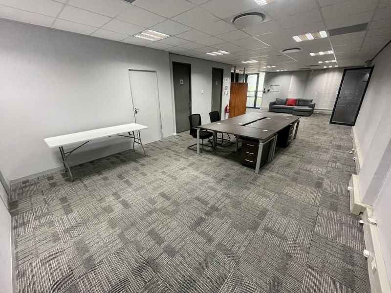 A spacious open-plan office area featuring carpet tile flooring, suspended ceiling with recessed lighting, and glass partition elements.