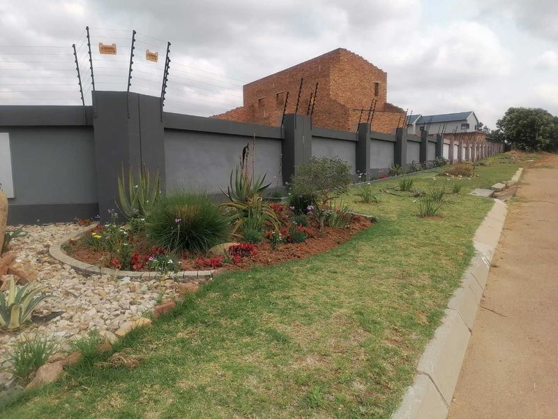 Street view of a residential property featuring a modern perimeter wall with integrated electric fencing and a well-maintained landscaped garden bed.