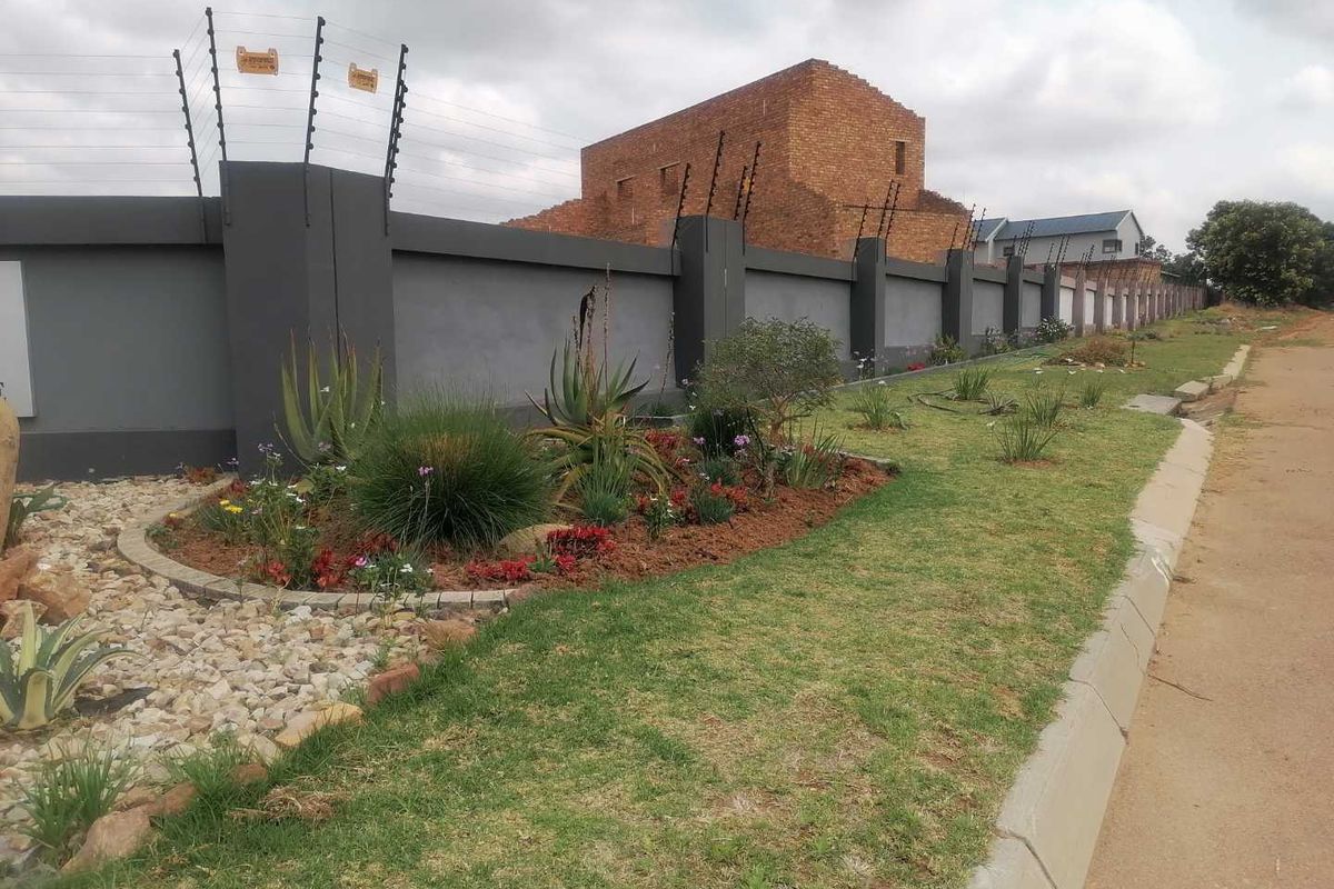 Street view of a residential property featuring a modern perimeter wall with integrated electric fencing and a well-maintained landscaped garden bed.