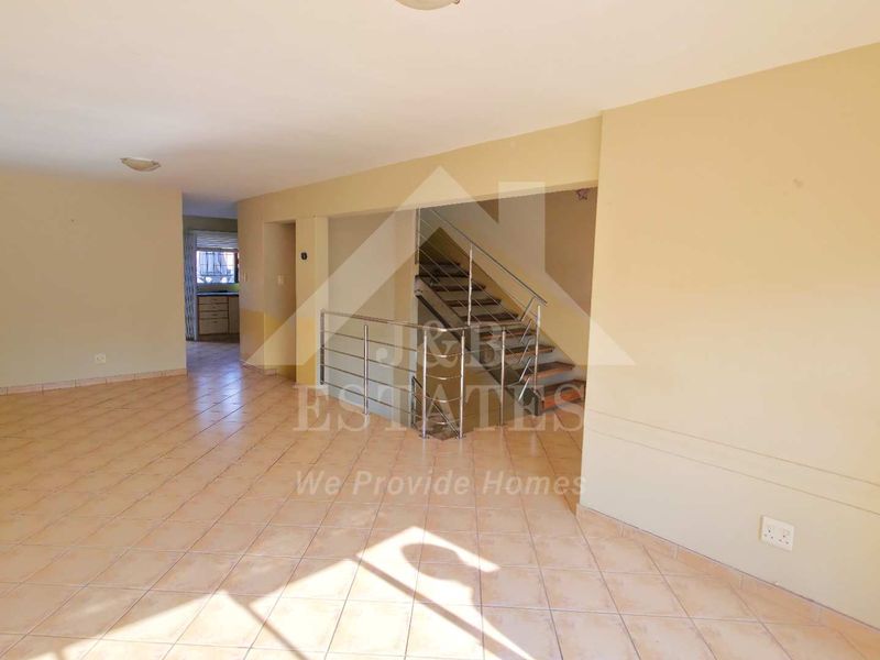 Spacious open-plan living area featuring tiled flooring and a central staircase with a metal balustrade, leading to the upper level.