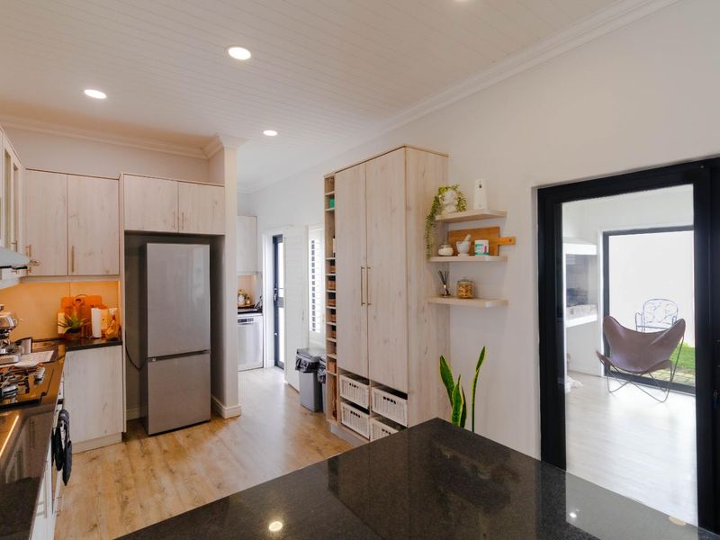 Modern kitchen featuring light wood cabinetry, dark stone countertops, recessed lighting, and a seamless transition to an adjacent outdoor area through a glass door.
