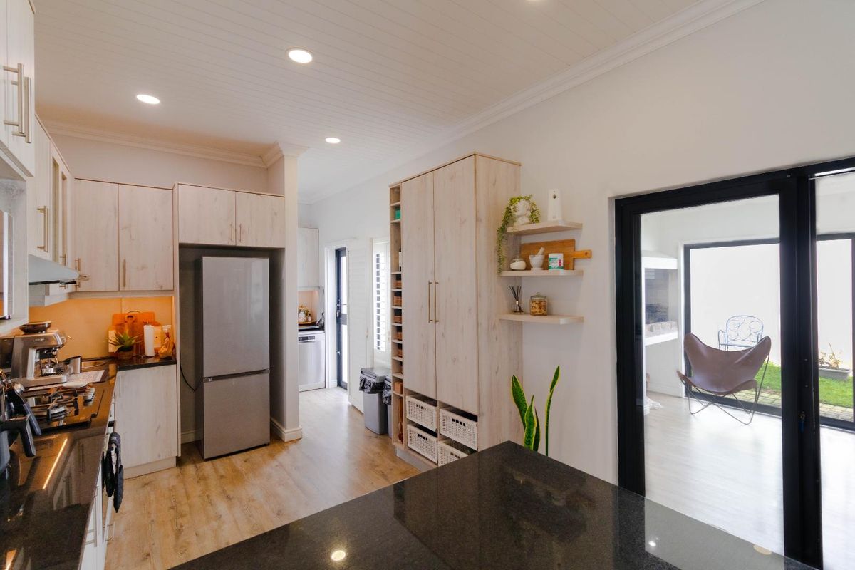 Modern kitchen featuring light wood cabinetry, dark stone countertops, recessed lighting, and a seamless transition to an adjacent outdoor area through a glass door.