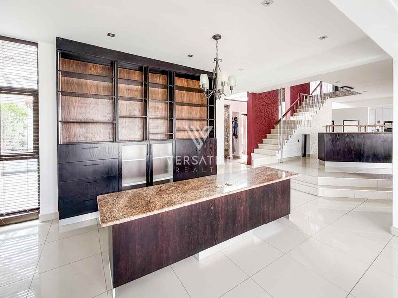 Spacious open-plan living area featuring built-in cabinetry, a granite-topped island, and a prominent staircase with modern metal railings.