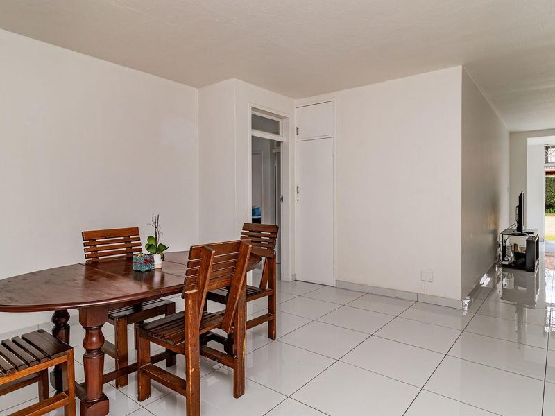 Open plan living and dining area featuring neutral white walls and polished floor tiles, with direct access to the exterior garden area.