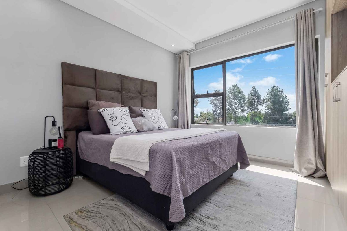 A bright and modern bedroom featuring tiled flooring, built-in cupboards, and a large window providing natural light and pleasant outdoor views.