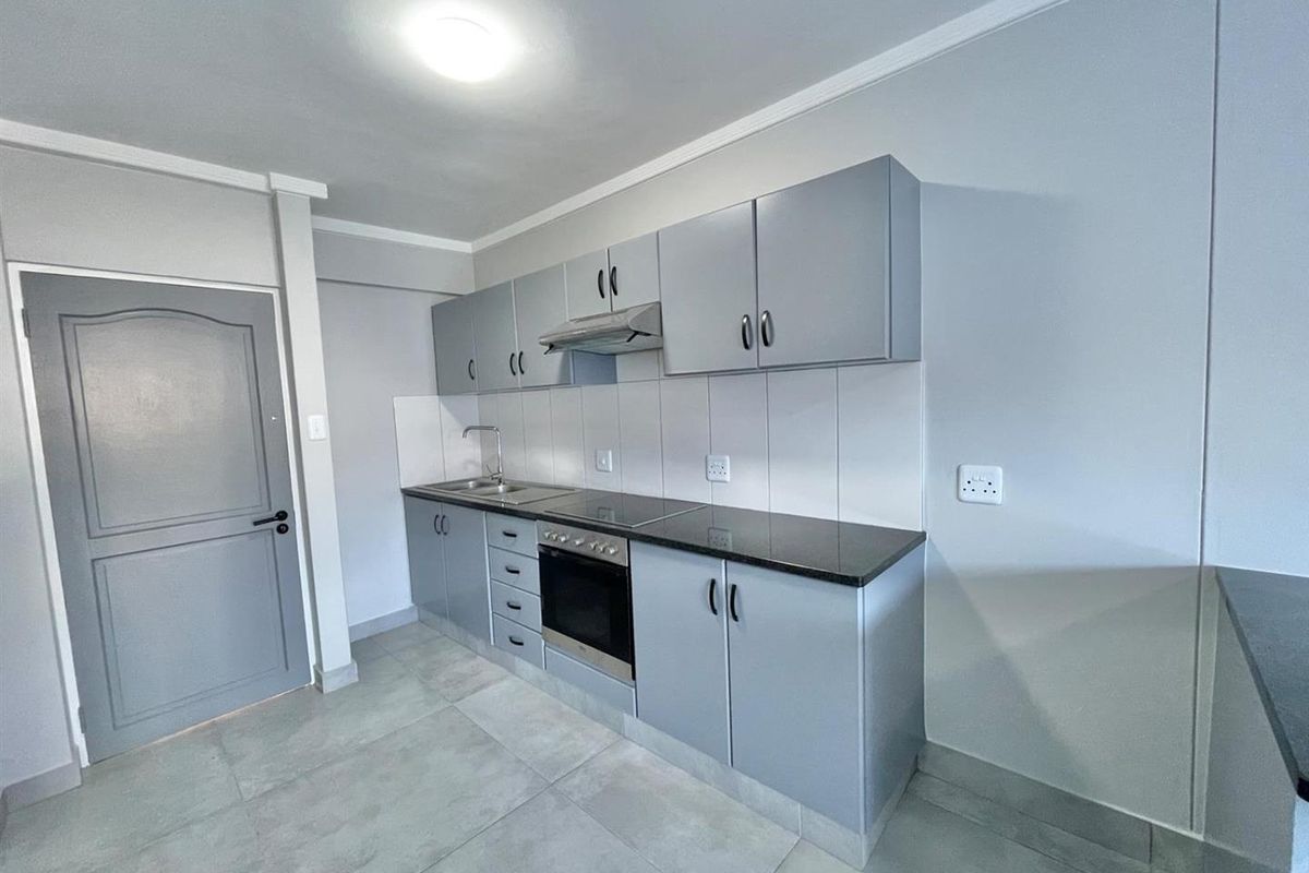 Modern kitchen featuring grey cabinetry, dark granite countertops, built-in oven, hob, extractor fan, and tiled flooring.