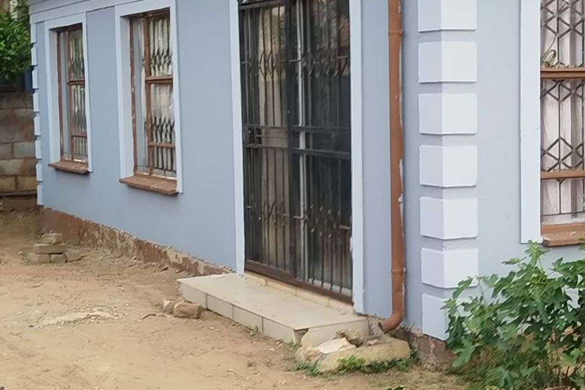 Exterior view of the rear building facade featuring tiled roofing, metal security gates, and burglar bars on the windows.