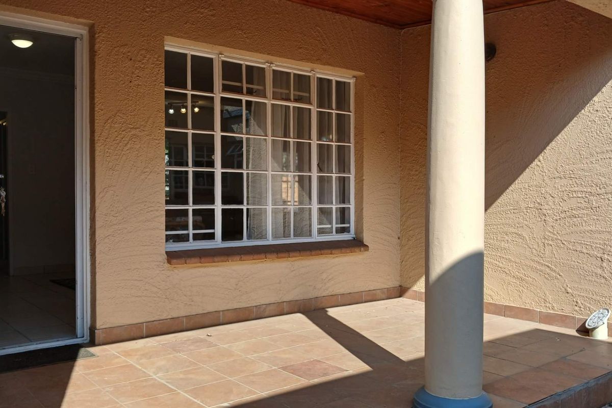 A covered patio area featuring tiled flooring, a structural column, and a multi-pane window looking into the interior of the cottage.