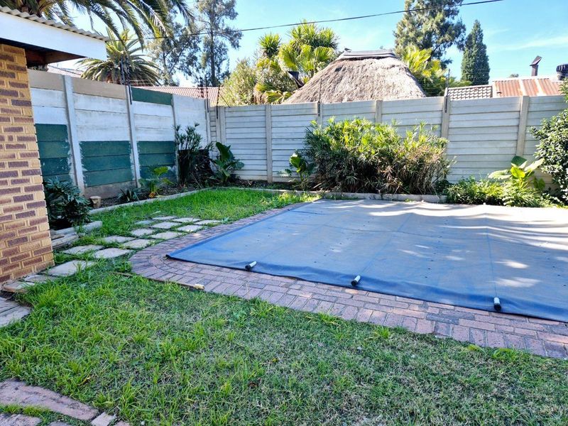 Outdoor pool area featuring a covered swimming pool, brick paving, and a precast concrete boundary wall with established garden greenery.
