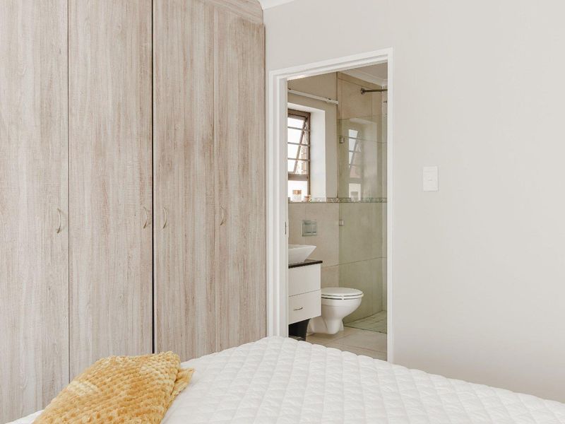 A well-maintained bedroom featuring built-in cupboards and direct access to a modern en-suite bathroom with a shower and vanity.