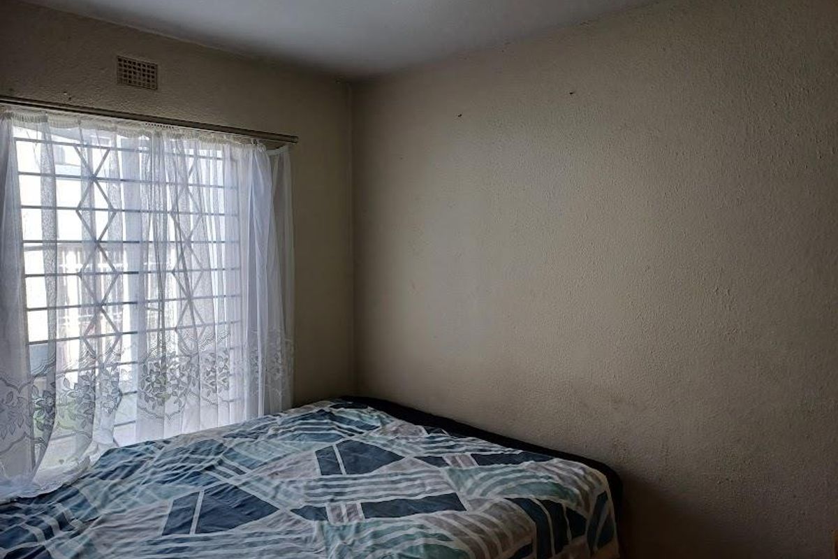 A bedroom featuring a window with a security gate and ventilation grille, requiring cosmetic updates to the wall finishes.