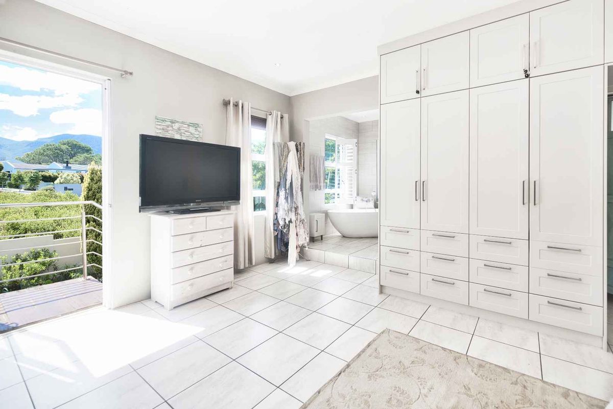 Spacious bedroom featuring extensive built-in cabinetry, tiled flooring, and direct access to a private balcony with scenic views, plus an en-suite bathroom.