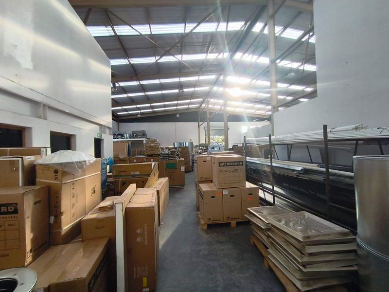 Spacious industrial warehouse unit featuring high exposed steel roof trusses, translucent roof panels for natural light, and durable concrete flooring.