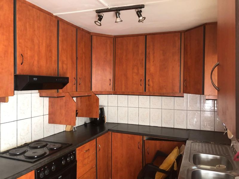 A dated kitchen featuring wood-look laminate cabinetry, dark countertops, ceramic tile backsplash, and built-in electric stove with extractor fan.