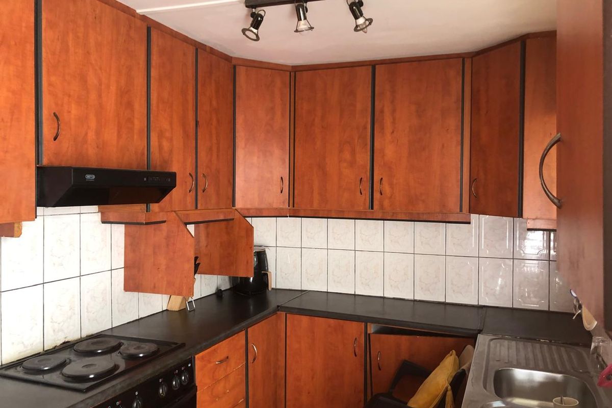 A dated kitchen featuring wood-look laminate cabinetry, dark countertops, ceramic tile backsplash, and built-in electric stove with extractor fan.