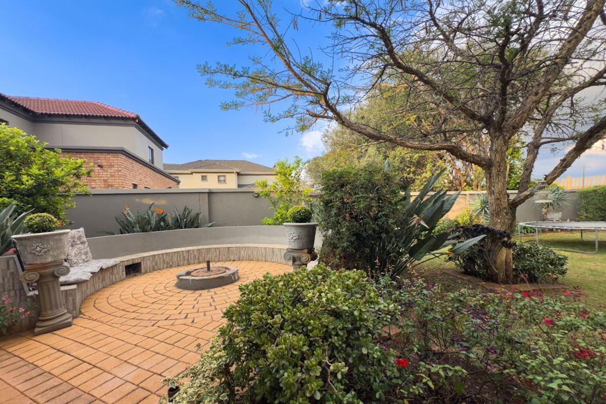 A landscaped rear garden featuring a circular paved patio area with a built-in fire pit and curved seating wall.