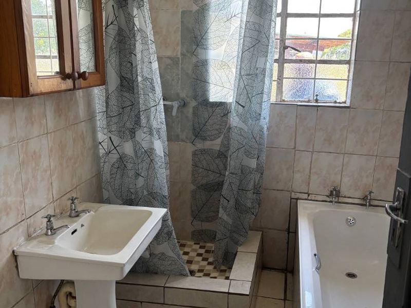A functional bathroom featuring a pedestal basin, a built-in bathtub, and a raised shower enclosure with tiled finishes throughout.