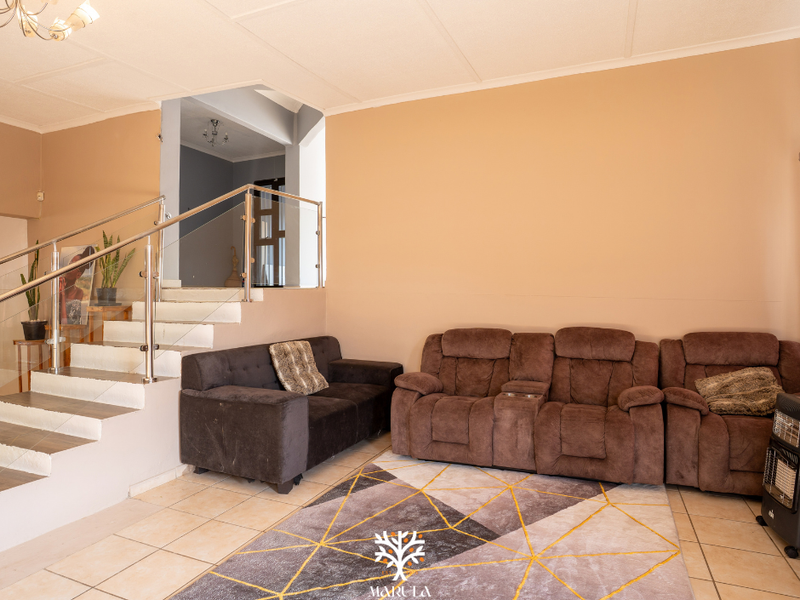Spacious living area featuring tiled flooring, a staircase with a modern stainless steel and glass balustrade, and neutral wall finishes.