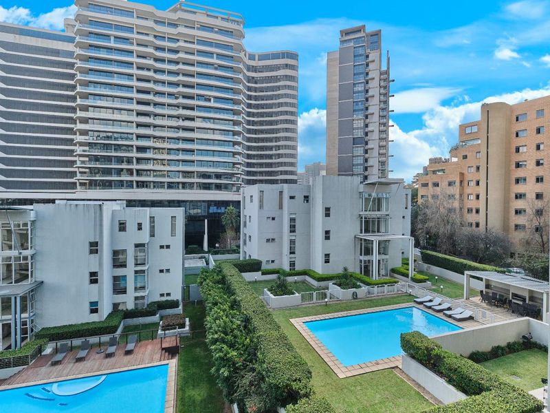 An elevated aerial view of the apartment complex featuring communal swimming pools, landscaped gardens, and a covered outdoor entertainment area.