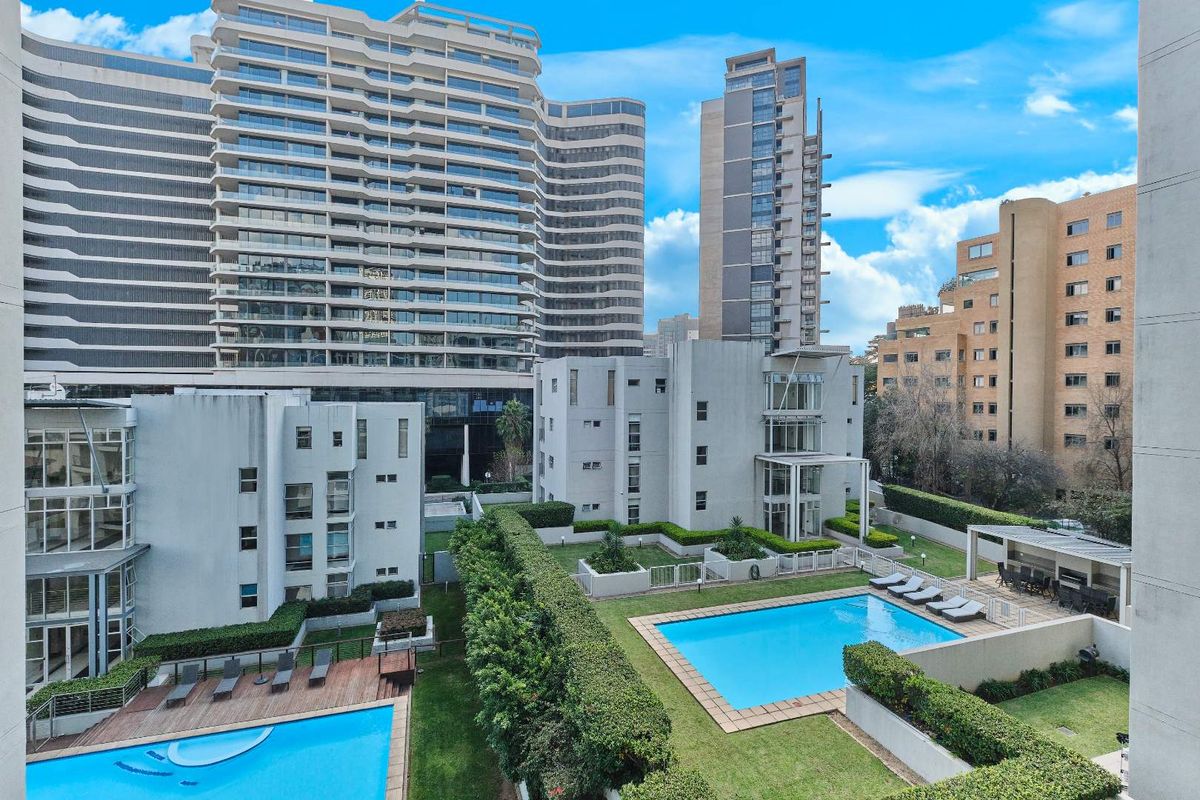 An elevated aerial view of the apartment complex featuring communal swimming pools, landscaped gardens, and a covered outdoor entertainment area.