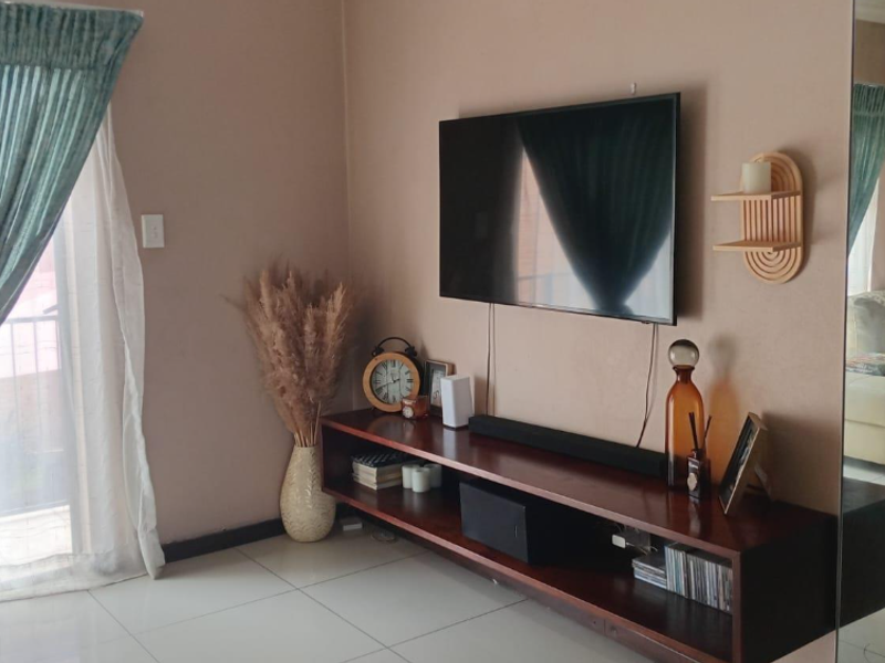 A living room featuring tiled flooring, a wall-mounted television, and a large mirror, with direct access to an outdoor area through a sliding glass door.