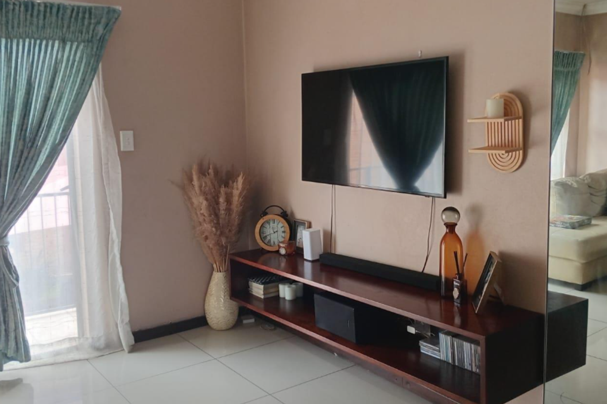 A living room featuring tiled flooring, a wall-mounted television, and a large mirror, with direct access to an outdoor area through a sliding glass door.