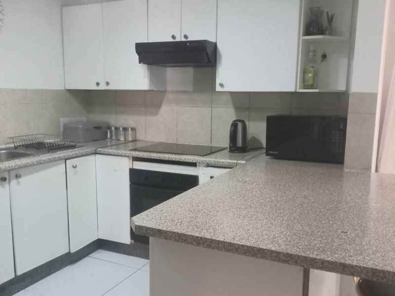 A functional kitchen featuring white cabinetry, laminate countertops, a built-in oven with hob, extractor fan, and tiled flooring.