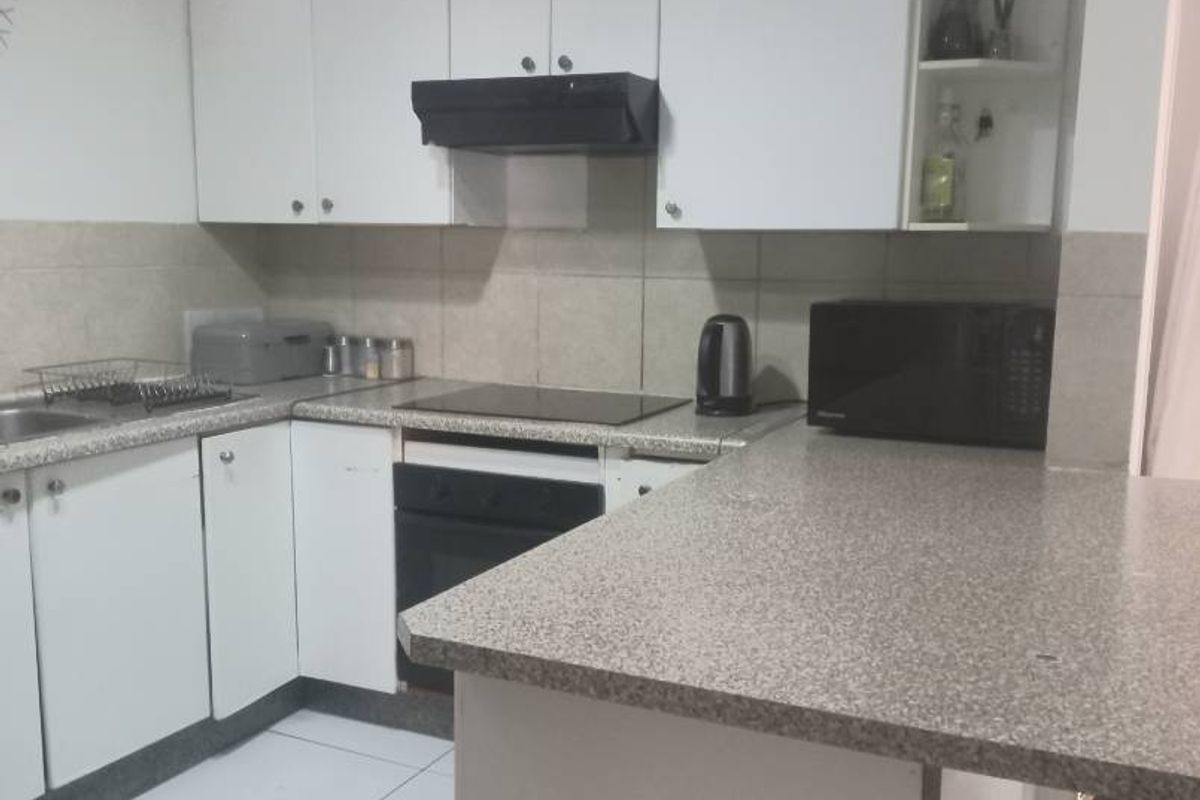 A functional kitchen featuring white cabinetry, laminate countertops, a built-in oven with hob, extractor fan, and tiled flooring.