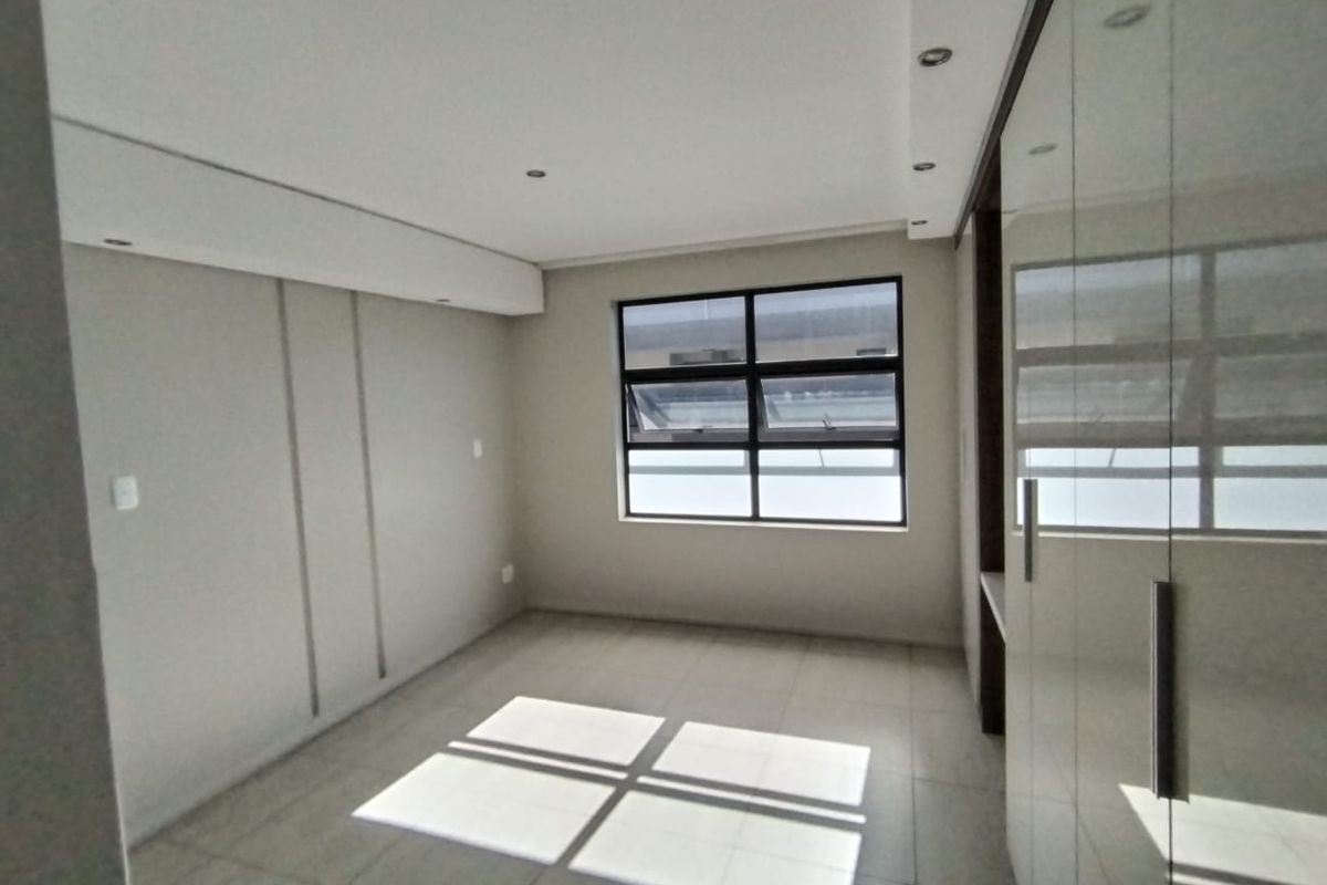 A bright, empty bedroom featuring neutral tiled flooring, recessed downlighting, and modern built-in cupboards with a glossy finish.