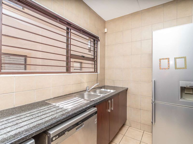 A functional scullery area featuring tiled walls, granite countertops, a double sink, and built-in cabinetry with security bars on the window.