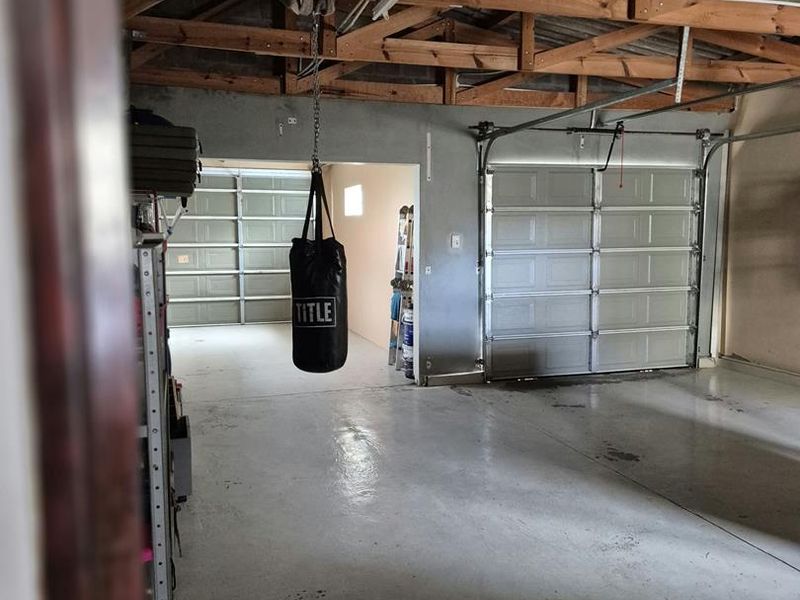 Spacious double garage featuring exposed timber roof trusses, sectional garage doors, and a durable epoxy-coated concrete floor.